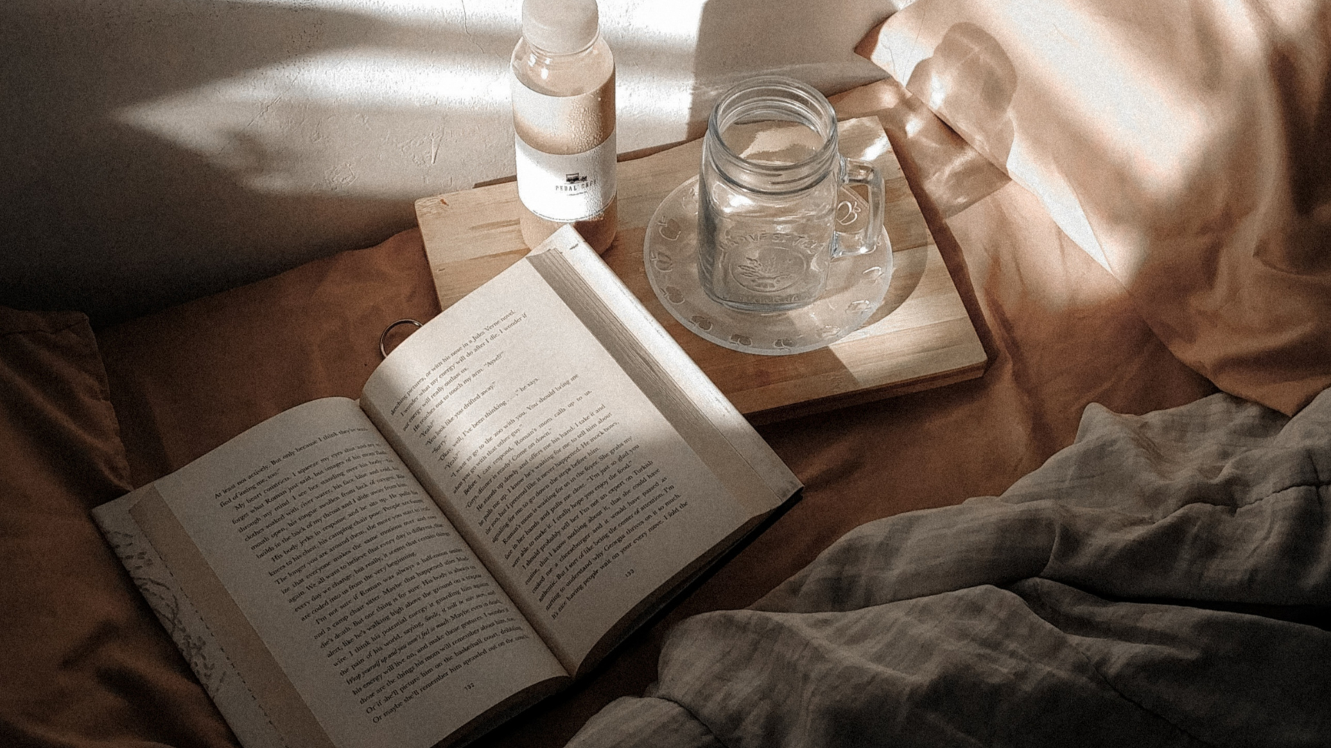 Open book on a wooden table with a glass of water and a candle, soft natural light filtering through curtains.