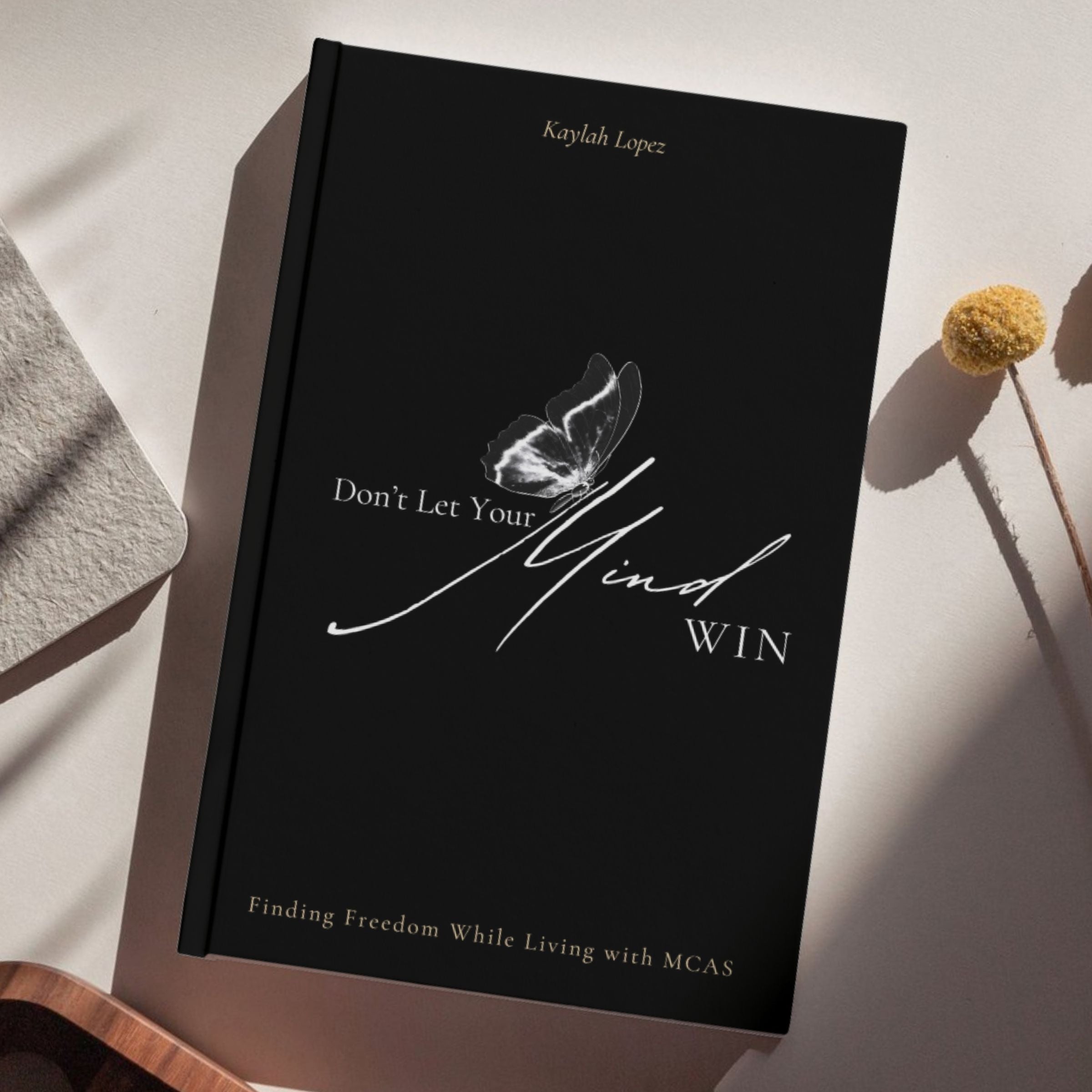 Book titled 'Don't Let Your Mind Win' by Kaylah Lopez on a light surface with a butterfly illustration.